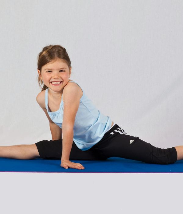 Happy child in a playful yoga pose on a blue mat.